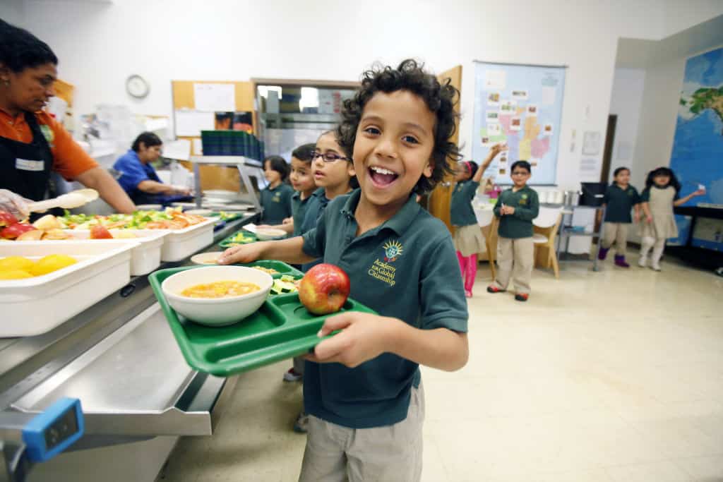 Jayden Ochoa, a first grader at the Academy of Global Citizenship in Chicago, smiles as he takes his full tray of food to his seat in the school's cafeteria Monday, May 13, 2013.  | Photo by J.Geil