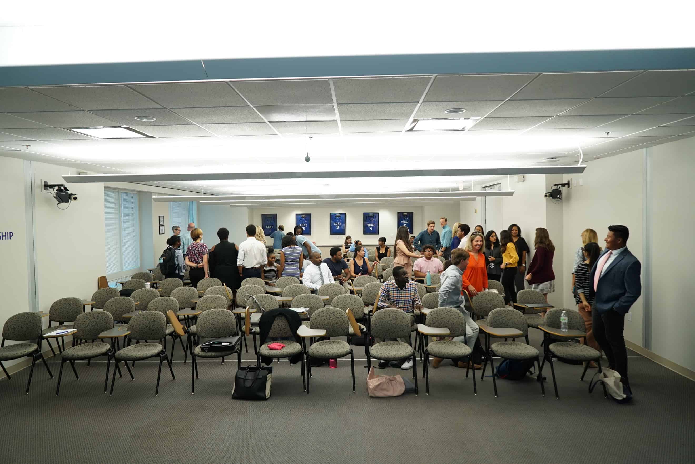 Students chat among desks in a lecture hall