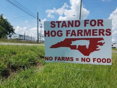 A sign reading STAND FOR FARMERS, NO FARMS = NO FOOD across the street from a meat packing plant