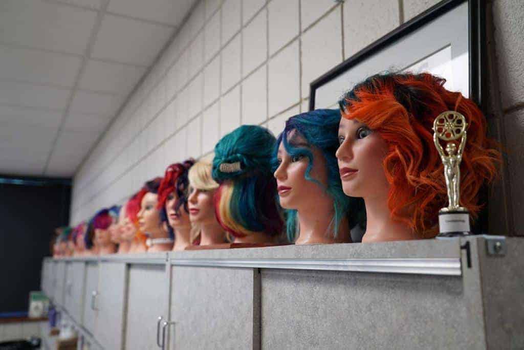 A row of cosmetology mannequins with multicolored hair sits atop a cabinet