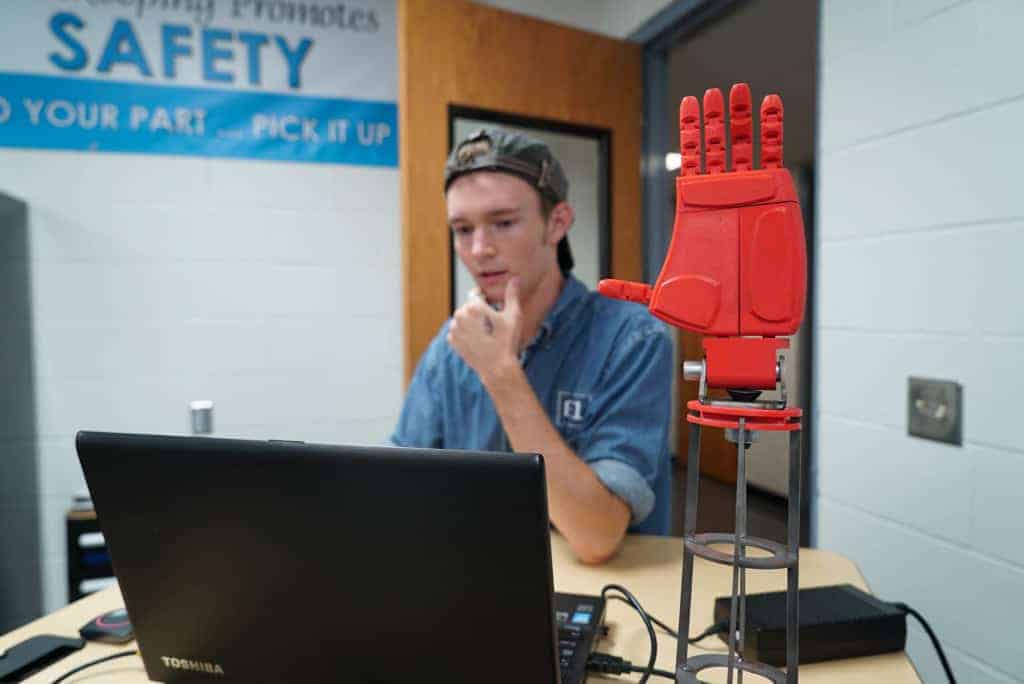 a student works on a computer behind a 3d printed plastic hand
