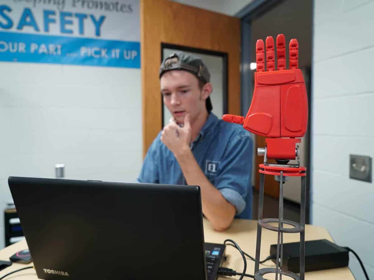 a student sits at computer behind 3D printed hand