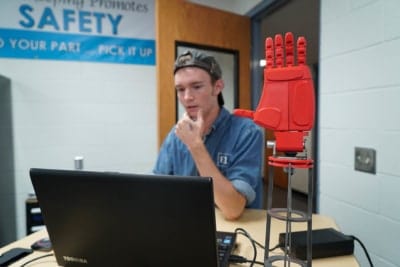 a student sits at computer behind 3D printed hand