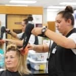 a student uses a blowdryer a patron's hair