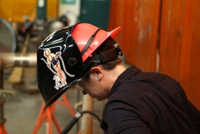 Woman looks down wearing welding helmet