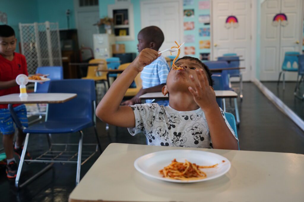 a small boy eating spaghetti in school cafeteria.