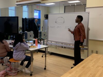 Dr. Williams writes on a whiteboard in front of a small class of elementary school students