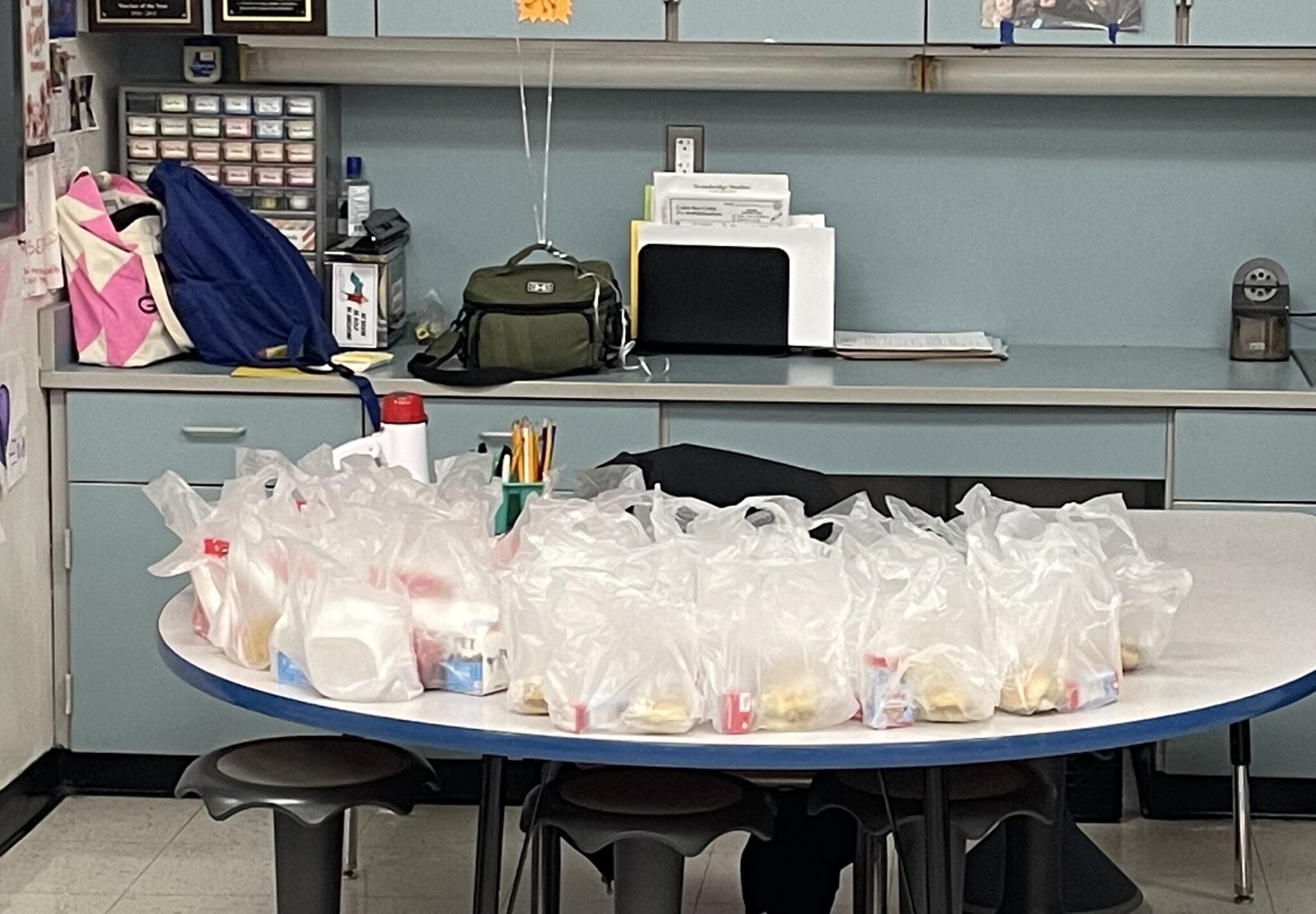 Several bags of breakfast items sit on a classroom table.