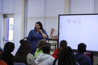 Woman teaching equation on whiteboard in frontof a class