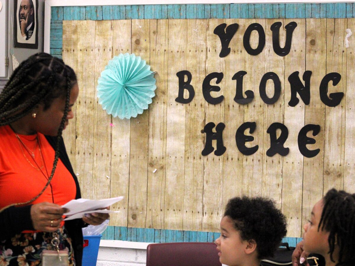 teacher in front of buildboard with three small students