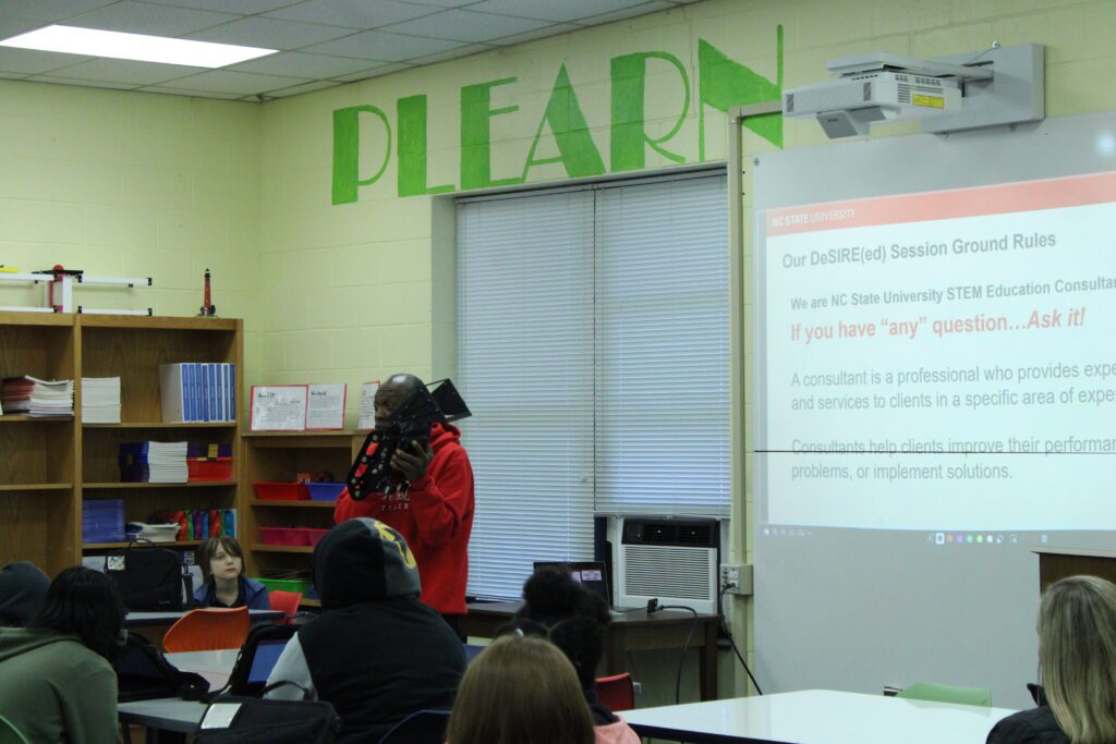 man in red hoodie holding robotic part in front of projector