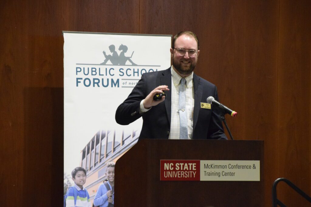 man standing at brown podium with clicker in hand