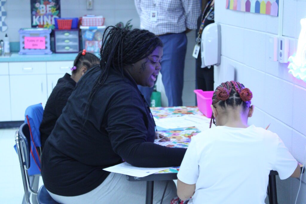 woman sitting at a desk between two small children with worksheets