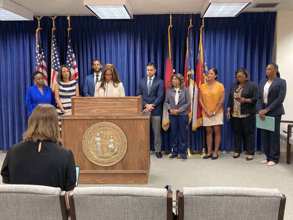 woman stands at a podium in front of North carolina and amaerican flag
