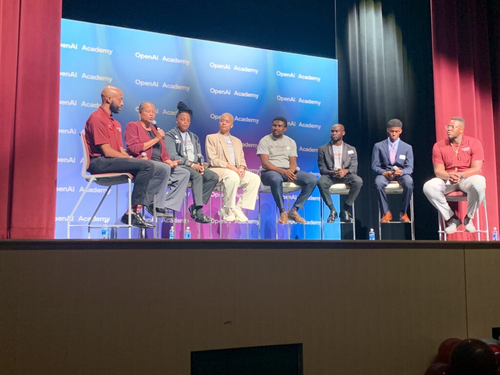 seven students sitting on stage in front of open ai academy back drop
