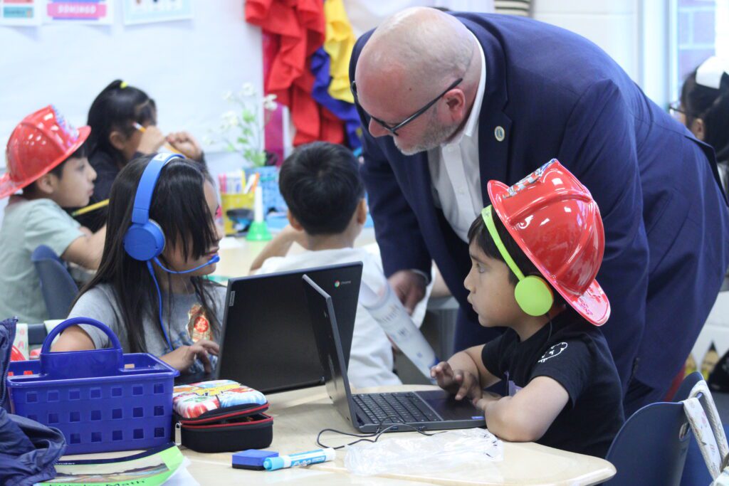 man kneels over students with headphones in