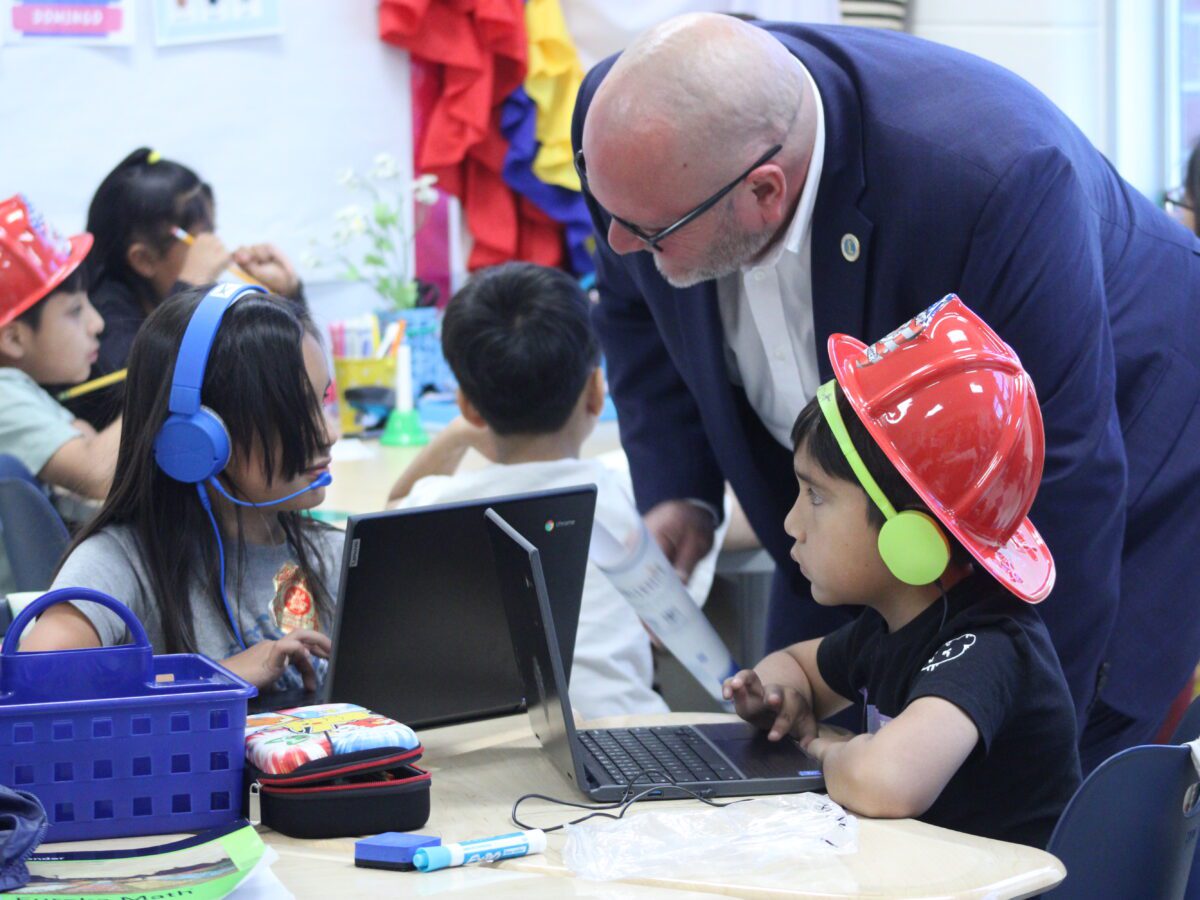 man kneels over students with headphones in