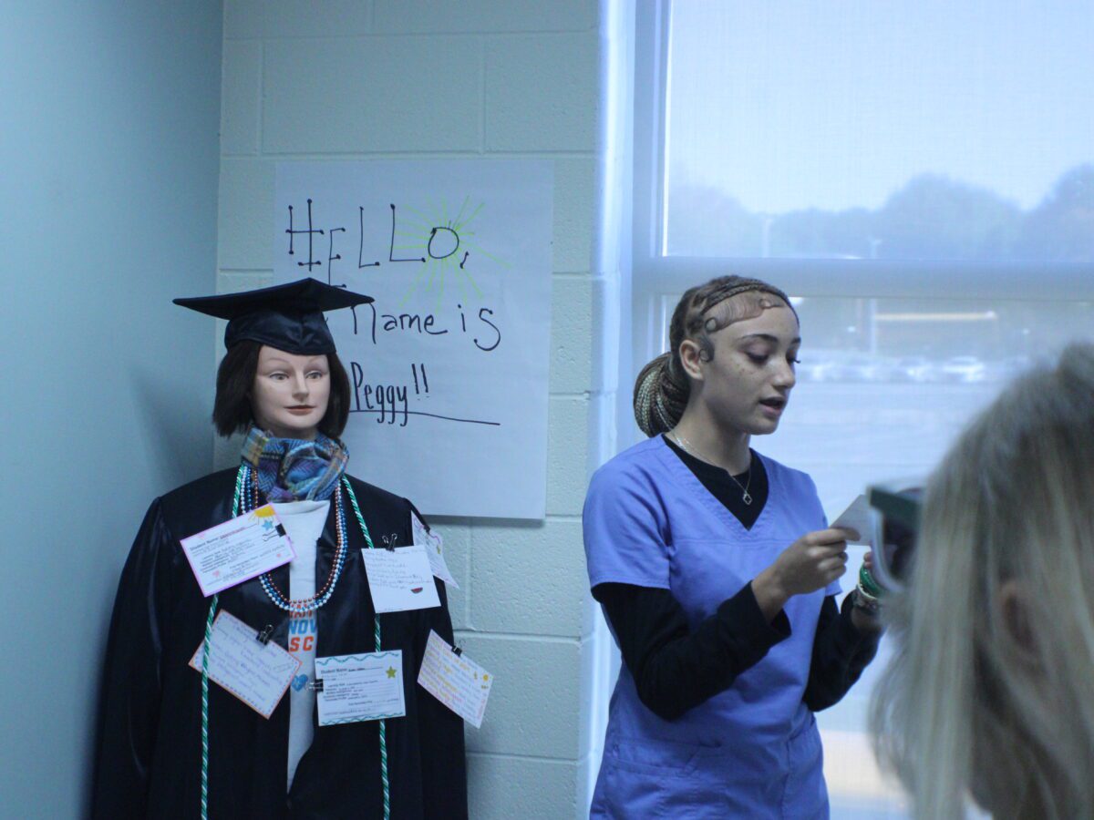 student in scrubs speaking in front of mannequin with notecards pinned to it