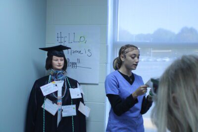 student in scrubs speaking in front of mannequin with notecards pinned to it