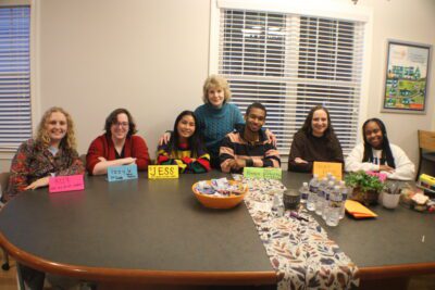 seven people sit and stand around an oval table with name tags