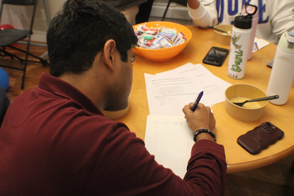 person sits at table and writes math equation next to empty paper bowl with a fork