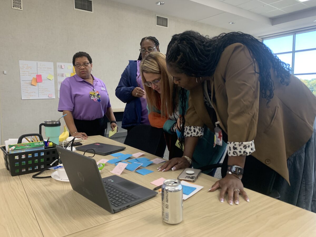 people standing over laptops and post it notes at a table