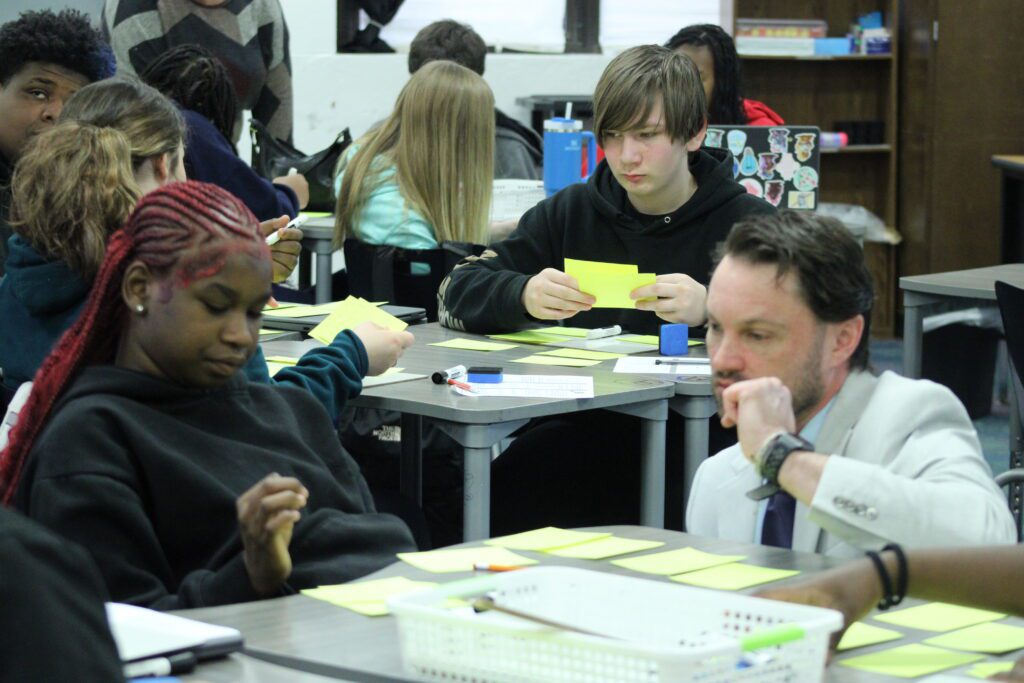 man kneeling at desk with students