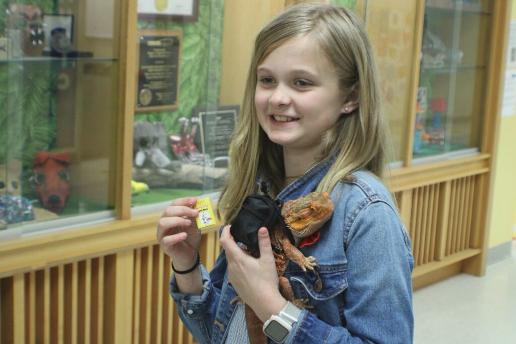 student holding a bearded dragon with a palm-sized diary of a wimpy kid book