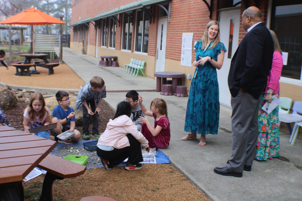 students touching rocs while sitting on a mat on the ground as adults watch