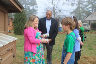 mo green standing with students and principal in front of chicken coup