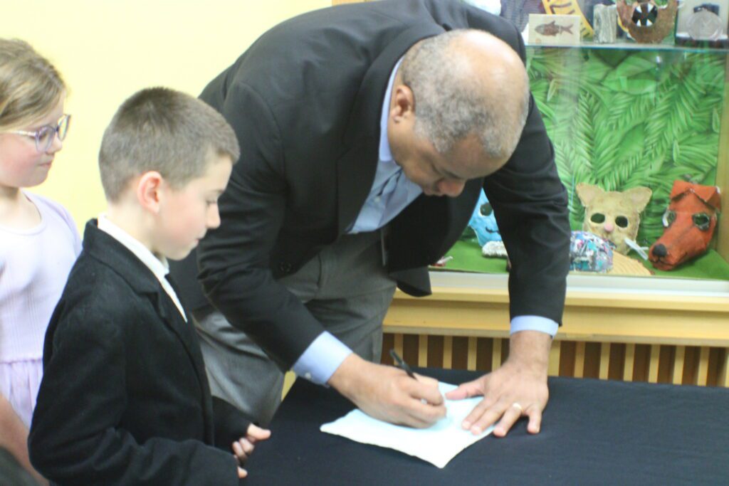 man signing a piece of paper in front of two children