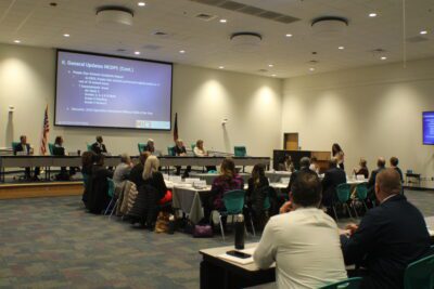 people sitting around a table in blue chairs looking to the right at a podium