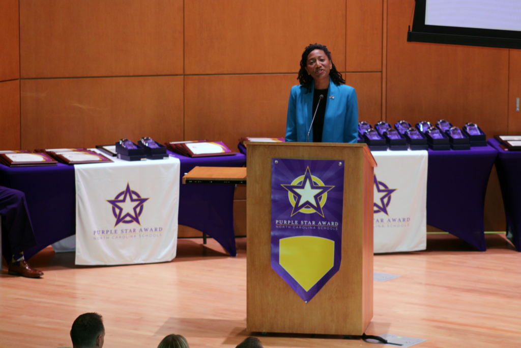 woman standing at a podium with a purple flag