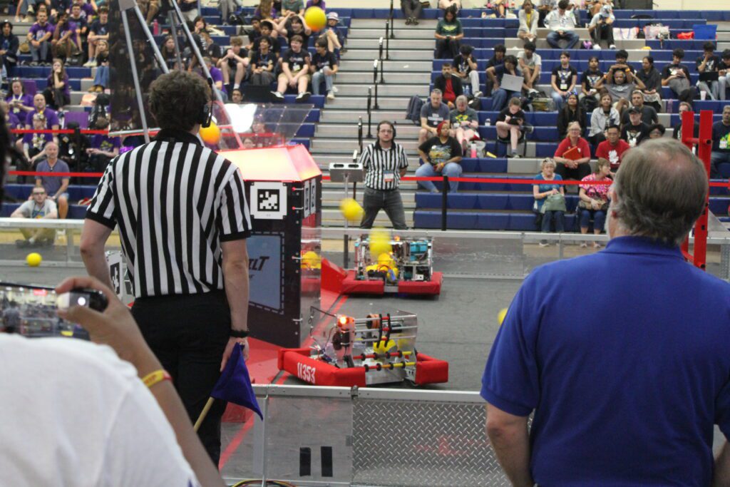 people in referee shirst standing on the opposite sides of a glass arena of flat remote powered robots