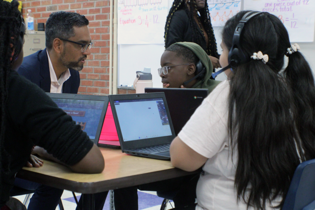 man sitting at desk with three students who have headphones on and laptops