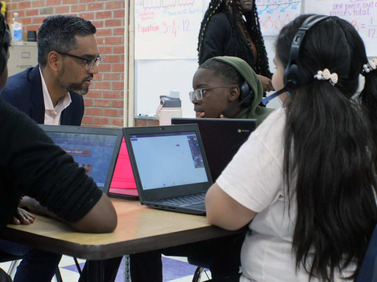 man sitting at desk with three students who have headphones on and laptops