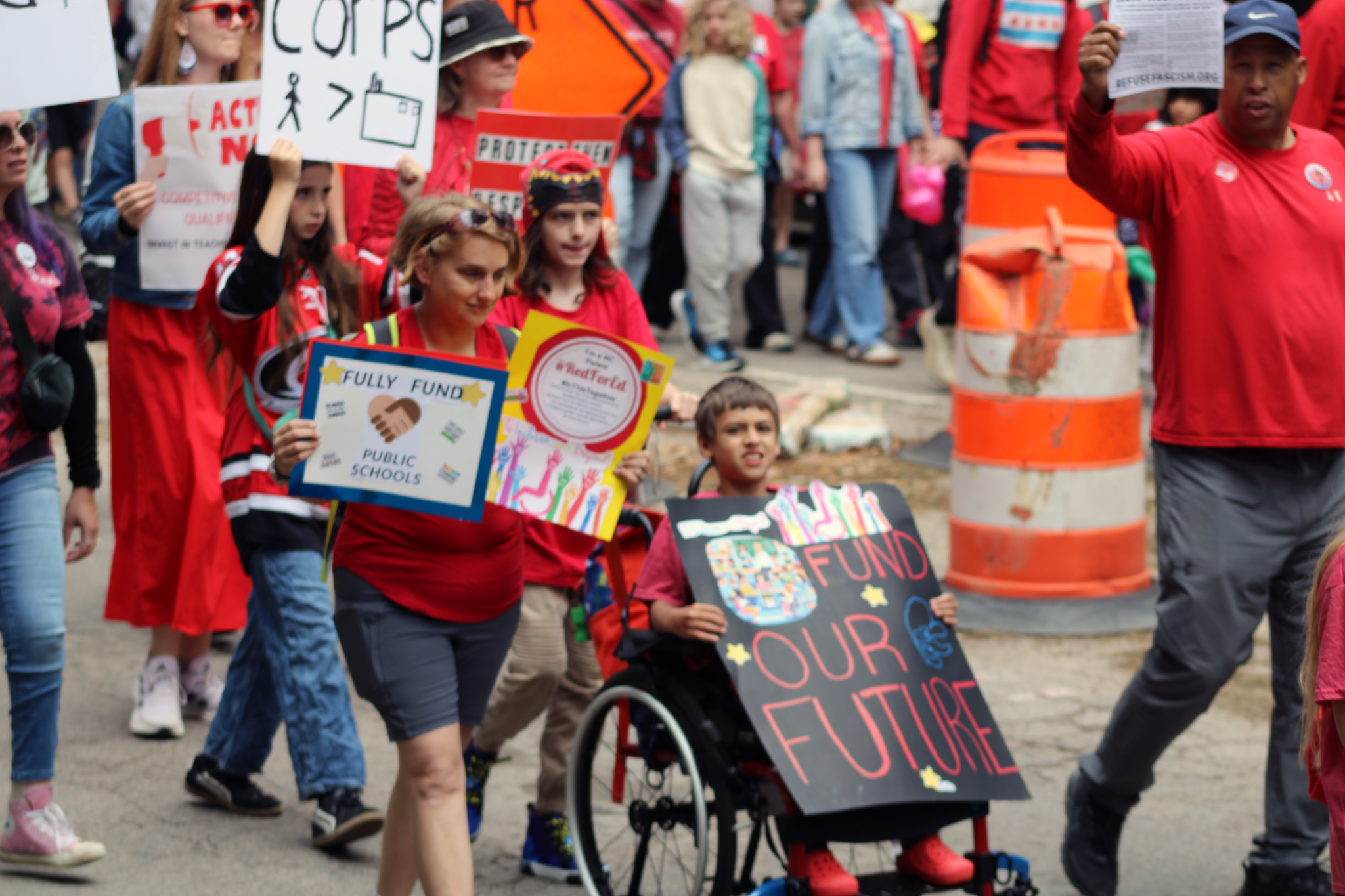 woman walking with child in a wheelchair holding a protest sign