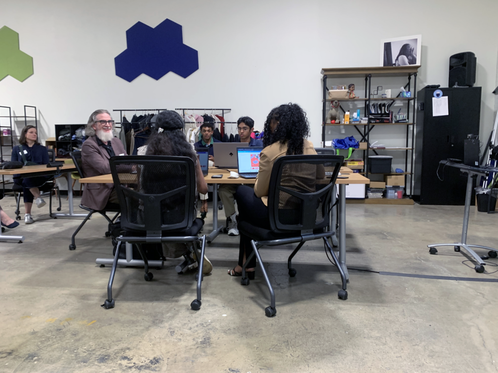 four students and adult male sitting at a table with laptops