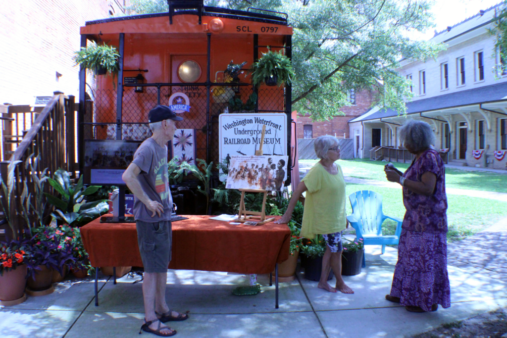 the front of the washington waterfront underground railroad museum with a orange table and three peopl in front of it