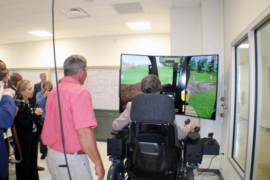 Two people looking at a hole animation on a screen one seated in a chair