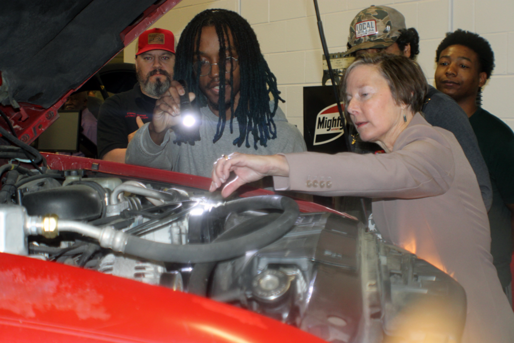 five people looking under hood of car with a flashlight