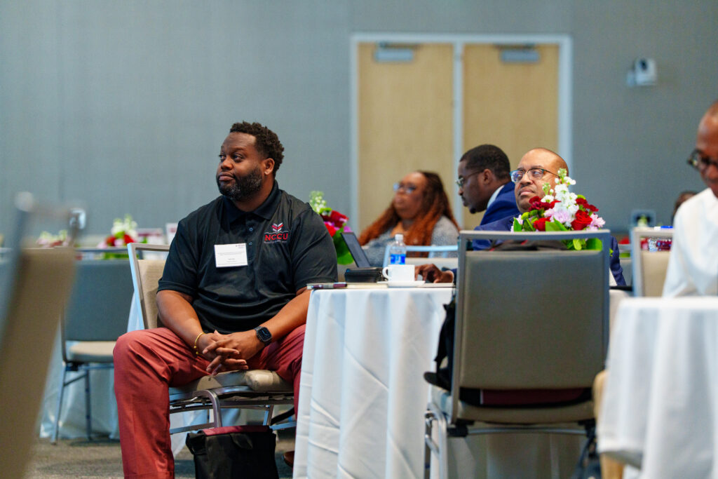 Attendees seated at tables in a conference room, attentively listening to a presentation.