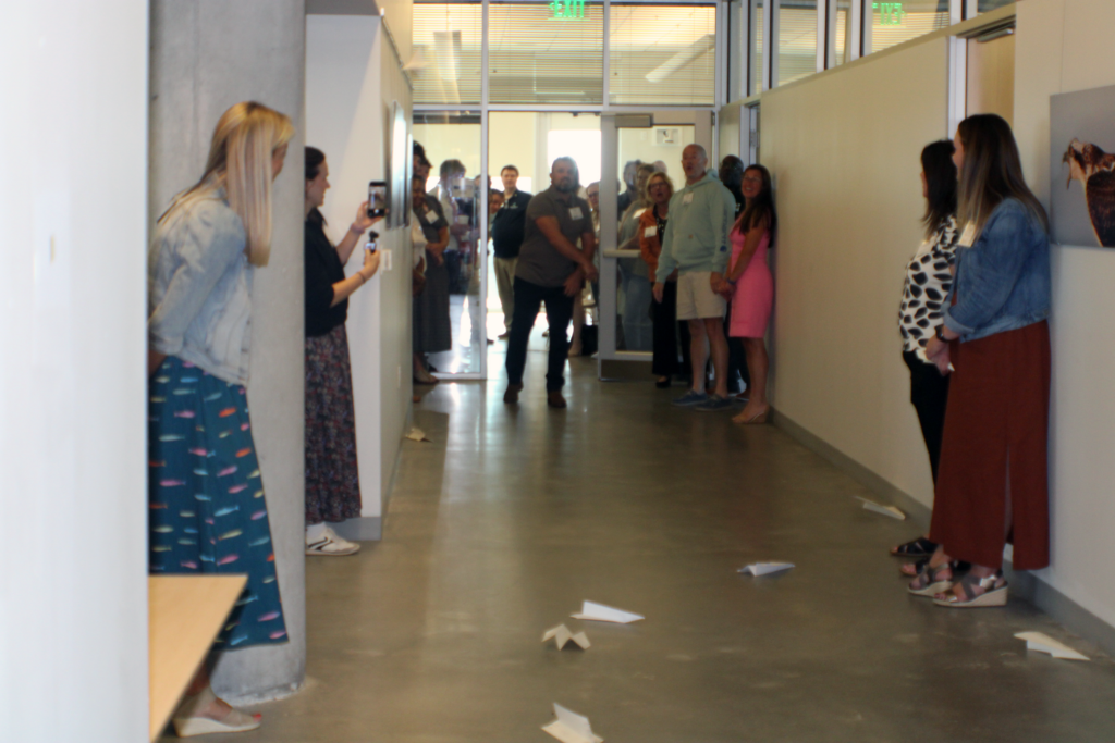 people watching white pieces of paper fly from one end of the hallway to the next