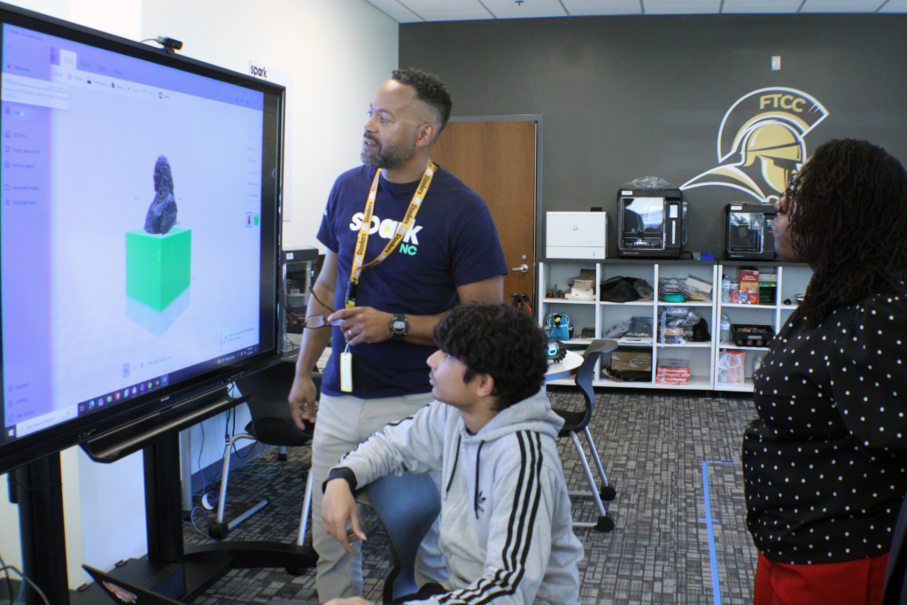 people looking at a 3d cube one a large screen in a classroom